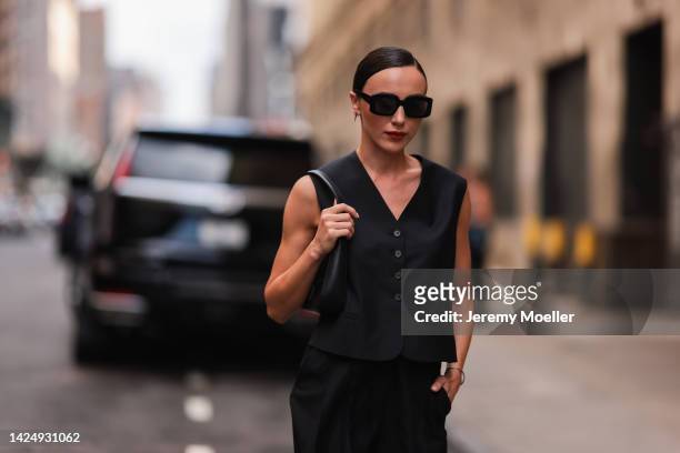 Mary Leest is seen wearing black square sunglasses, black sleeveless/buttoned gilet, black shiny leather shoulder bag and a black large suit pants,...