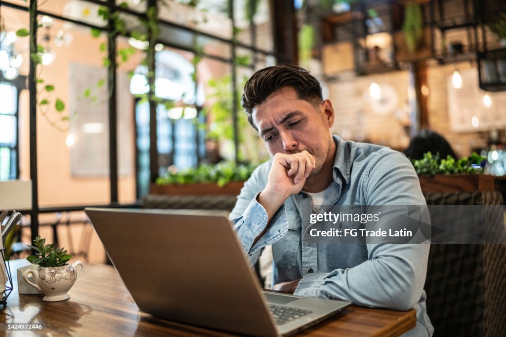 Worried mid adult businessman using laptop in a coffee shop