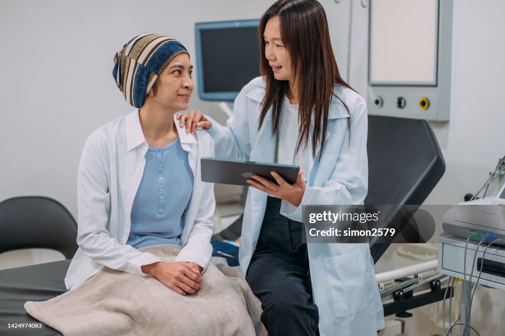 An Asian female gynecologist talking to her patient about her cancer test results on an electronic wireless tablet