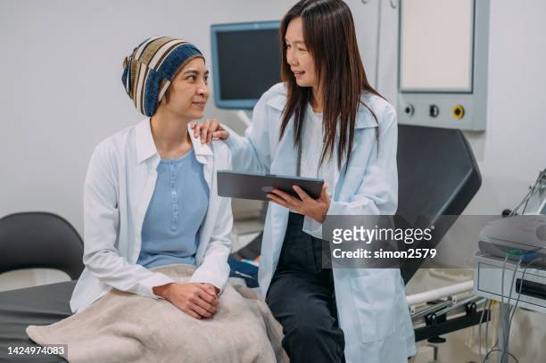 an asian female gynecologist talking to her patient about her cancer test results on an electronic wireless tablet - leukemia stock pictures, royalty-free photos & images