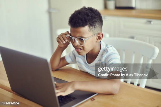 little african kid boy in glasses looks at the laptop screen, squints, try to read information, does not see, has vision problems. visual impairment due to excessive usage of modern wireless tech concept - alex boys stockfoto's en -beelden