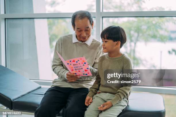 senior male asian patient reading a get well card with his grandkid sitting beside him at hospital ward. - get well card stockfoto's en -beelden