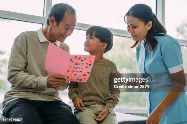an asian senior man received a get well card from his grandson sitting beside him at hospital ward. - get well card stockfoto's en -beelden