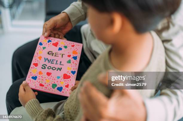 a boy gives a handmade card to his grandfather at hospital ward. grandfather arm around his grandkids and reading a get well card . he sitting beside him at hospital ward. - get well card stockfoto's en -beelden