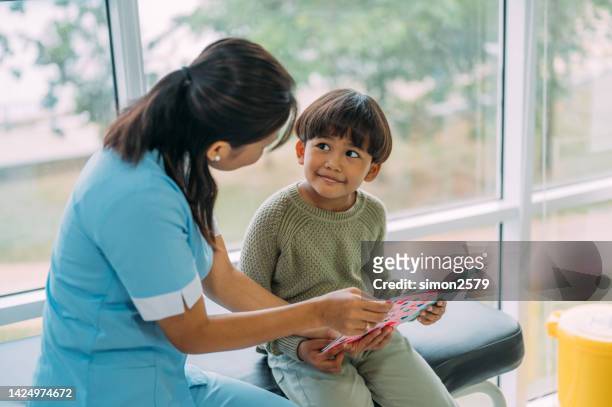 ein asiatisches kind erhielt eine get well-karte von einem gesundheitspersonal. sie saß neben ihm auf der krankenhausstation. - get well soon stock-fotos und bilder