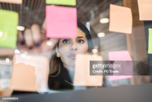 mujer joven escribiendo en post it en la oficina - apuntar fotografías e imágenes de stock