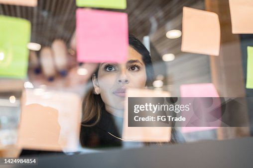 Jeune femme écrivant en post-it au bureau Jeune femme écrivant en post-it au bureau