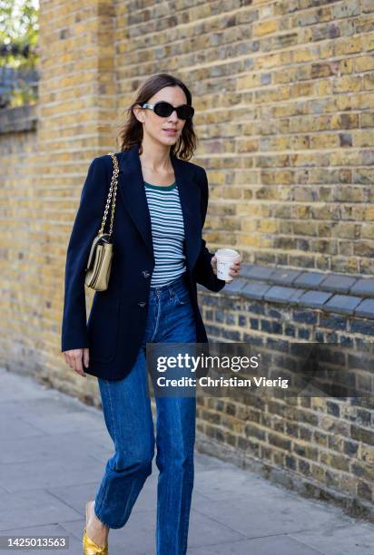 Alexa Chung wears navy blazer, denim jeans, striped shirt, Chanel bag, yellow heels outside Nensi Dojaka during London Fashion Week September 2022 on...