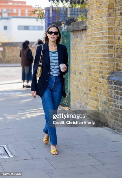 Alexa Chung wears navy blazer, denim jeans, striped shirt, Chanel bag, yellow heels outside Nensi Dojaka during London Fashion Week September 2022 on...