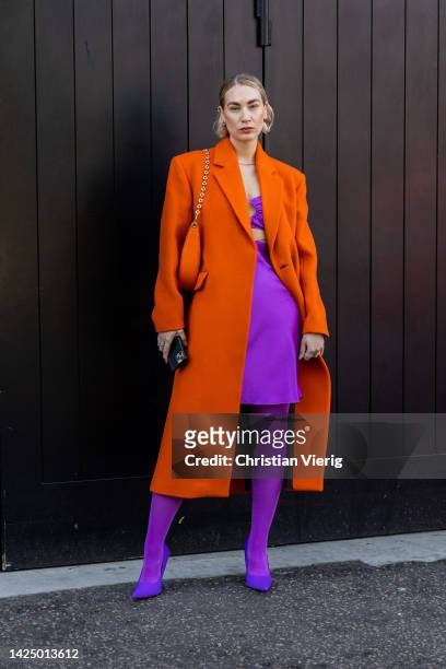 Guest wears orange wool coat, bag, purple skirt, tights, heels outside Nensi Dojaka during London Fashion Week September 2022 on September 18, 2022...