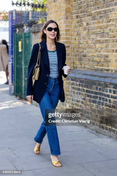 Alexa Chung wears navy blazer, denim jeans, striped shirt, Chanel bag, yellow heels outside Nensi Dojaka during London Fashion Week September 2022 on...