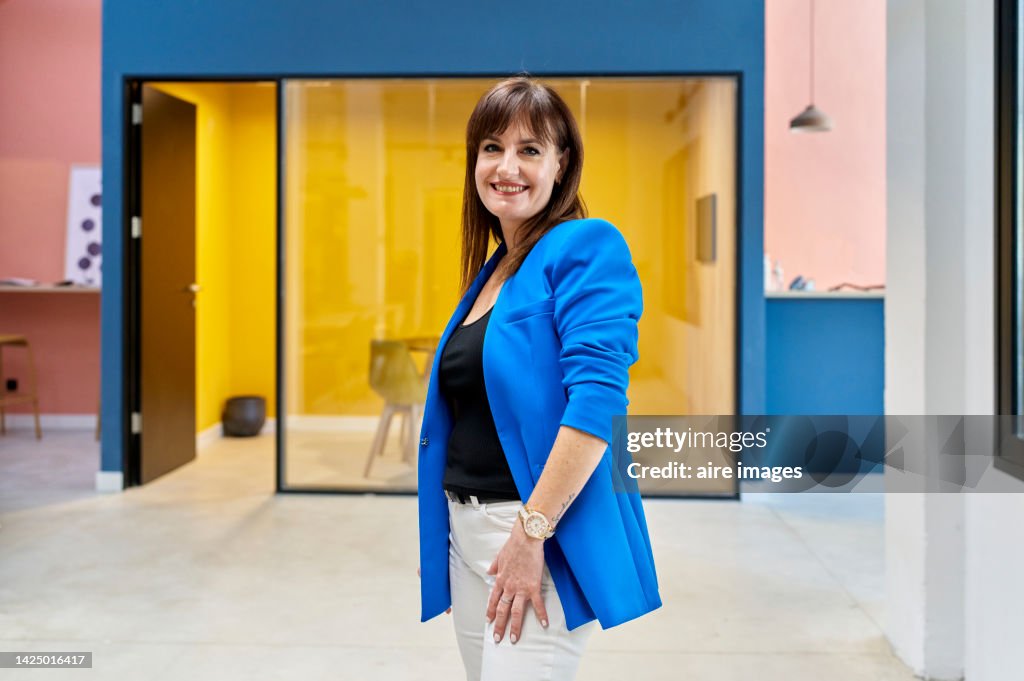 Smiling elegantly dressed middle-aged woman standing smiling and looking at the camera inside her office.