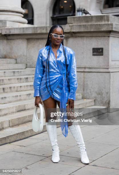 Guest wears blue glitter dress, white Coperni bag, white laced boots outside Halpern during London Fashion Week September 2022 on September 18, 2022...