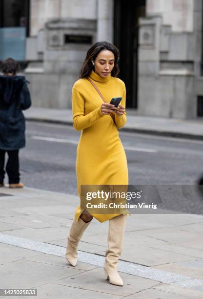 Guest wears mustard yellow dress, beige boots outside Halpern during London Fashion Week September 2022 on September 18, 2022 in London, England.