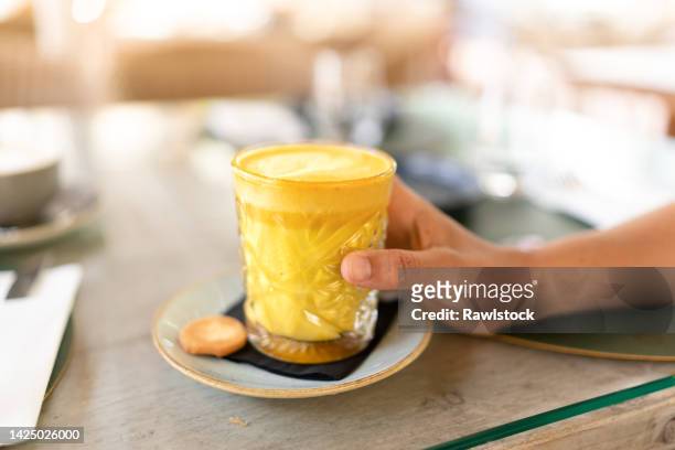 a hand holding a turmeric latte drink - yellow milk stock-fotos und bilder