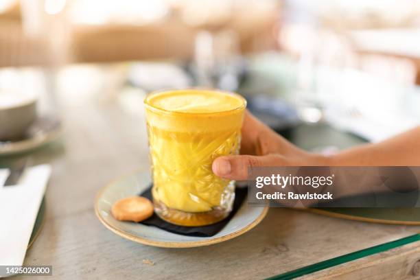 a hand holding a turmeric latte drink - turmeric stock pictures, royalty-free photos & images