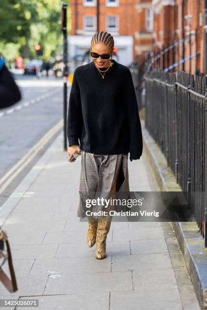 Model Adwoa Aboah wears checkered skirt with slit, black jumper, boots with snake print outside 16Arlington during London Fashion Week September 2022...