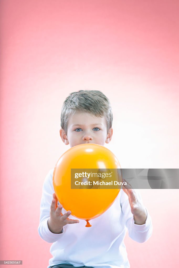 Boy hiding behing a balloon looking innocent