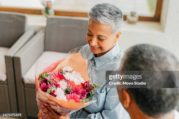 mann überraschen frau mit blumenstrauß für die liebe, älteres paar bei der feier der hochzeit und hochzeitstag im haus. glückliche, lächelnde und ältere menschen mit geschenk, um den ruhestand zu hause zu feiern - danke blumen stock-fotos und bilder