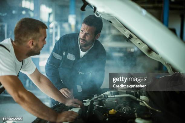automechaniker sprechen während der arbeit an überhitzten automotor in einer werkstatt. - auto mechaniker stock-fotos und bilder