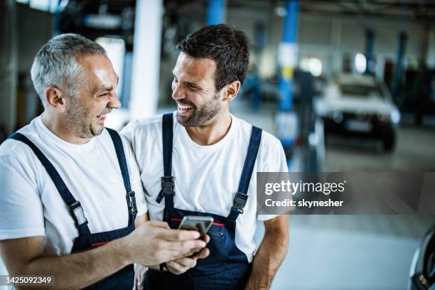 cheerful auto mechanics using cell phone in a workshop. - repairman phone stock pictures, royalty-free photos & images