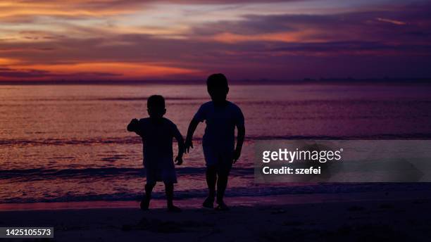 children silhouetted on beach - purple sunset stock pictures, royalty-free photos & images