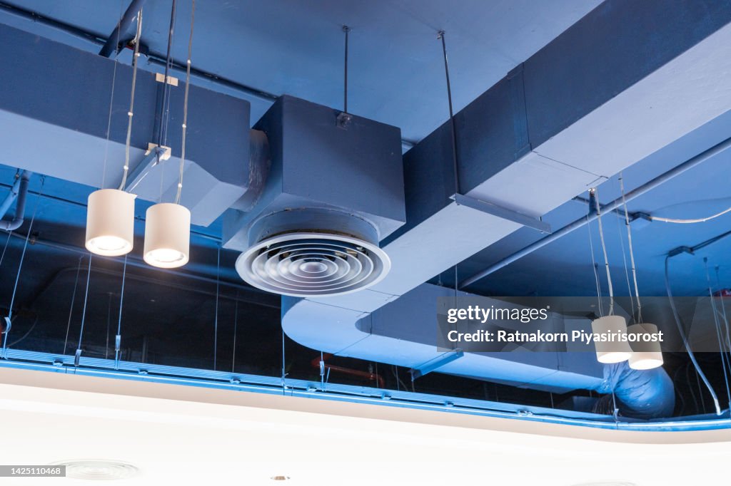 Bare ceiling with air duct, CCTV, air conditioner pipe and fire sprinkler system on white ceiling wall. Air flow and ventilation system. Ceiling lamp light with opened light. Interior architecture.