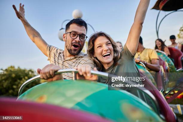 young carefree couple having fun on rollercoaster ride at amusement park. - amusement park ride stockfoto's en -beelden