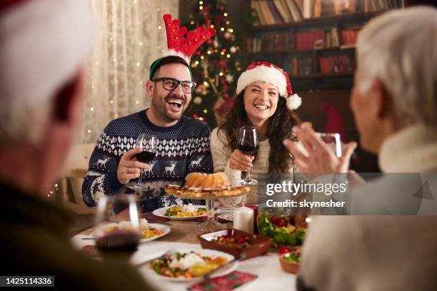 young happy couple talking to seniors during christmas dinner time at home. - christmas dinner stock pictures, royalty-free photos & images