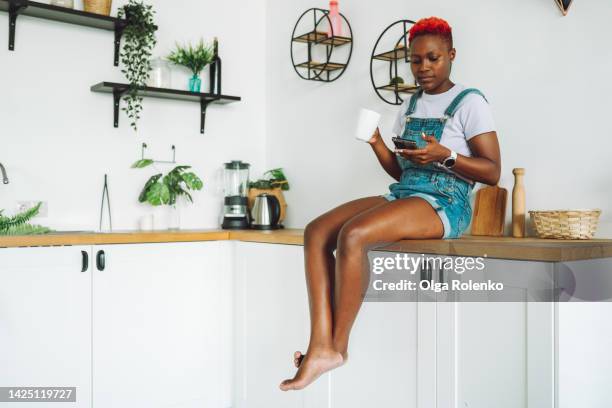 watching movies and listen to music online. african american woman and her digital routing with coffee and movies on weekends - red jumpsuit stock pictures, royalty-free photos & images