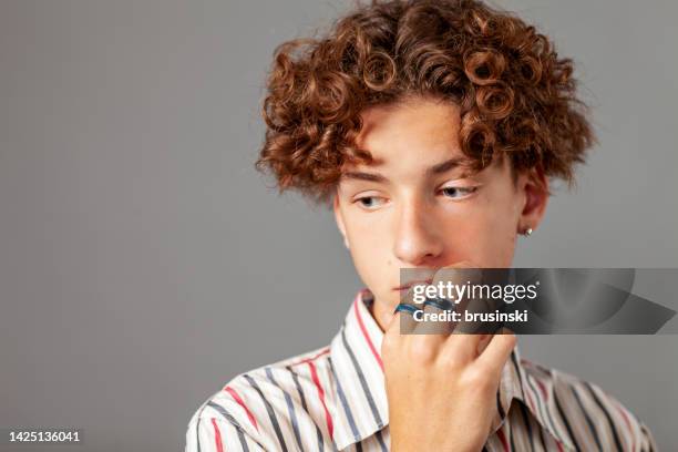 portrait en gros plan en studio d’un adolescent de 15 ans avec une boucle d’oreille dans une chemise rayée sur fond gris - boucle doreille photos et images de collection