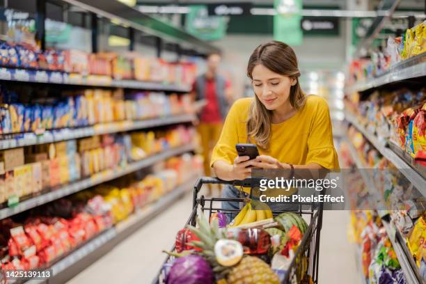 purchasing goods with smartphone at grocery store - market retail space stockfoto's en -beelden