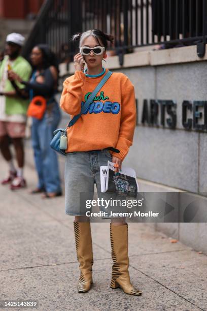 Val seen wearing an orange pullover with blue pattern, denim shorts and boots, outside coach during New York Fashion Week on September 12, 2022 in...