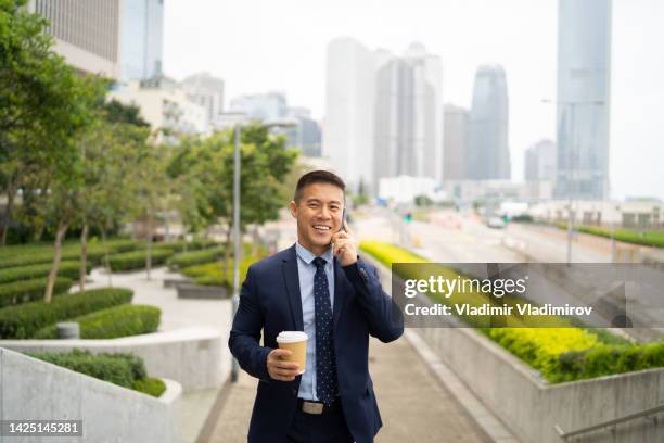 geschäftsmann, der mit kaffee zur arbeit geht, während er am telefon telefoniert - philippinischer abstammung stock-fotos und bilder