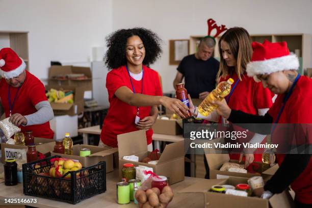 group of multi-ethnic volunteers working in charitable foundation, packing donation boxes - charitable foundation stockfoto's en -beelden