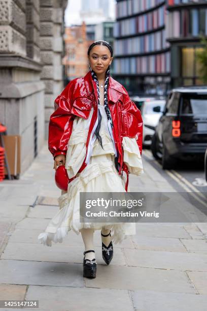 Griff wears red vinyl jacket, creme white ruffled dress, black platform shoes outside Simone Rocha during London Fashion Week September 2022 on...