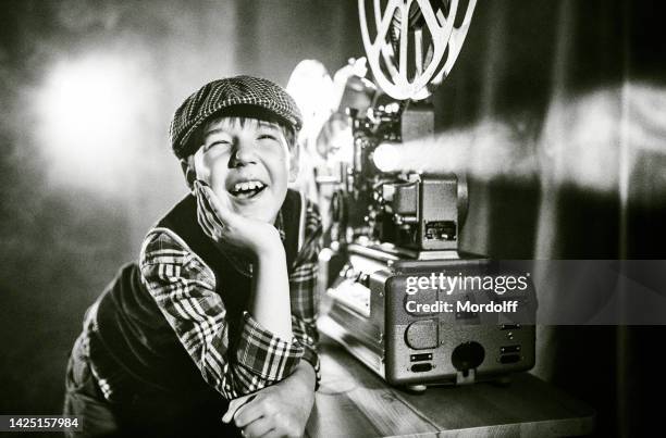 joyful boy film projectionist in old-fashion cap is watching film using old cinema projector - cinema projector stock pictures, royalty-free photos & images