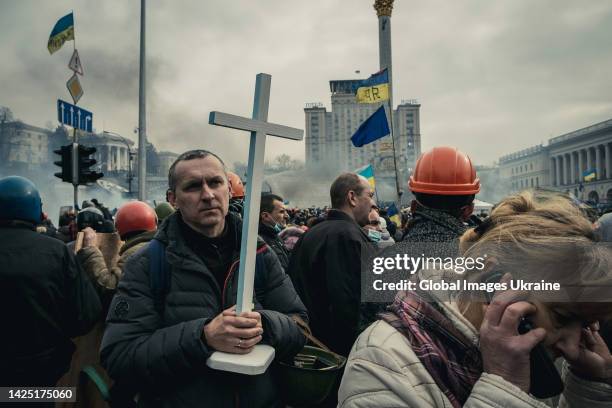 Man holds a cross standing amid protesters during the Revolution of Dignity on Maidan Nezalezhnosti on February 19, 2014 in Kyiv, Ukraine. A wave of...