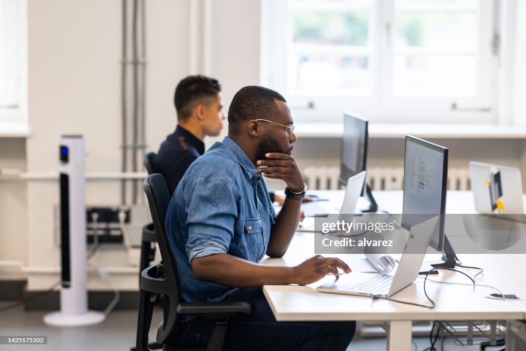 Zwei multirassische Männer, die an Desktop-Computern in einem Coworking-Büro arbeiten