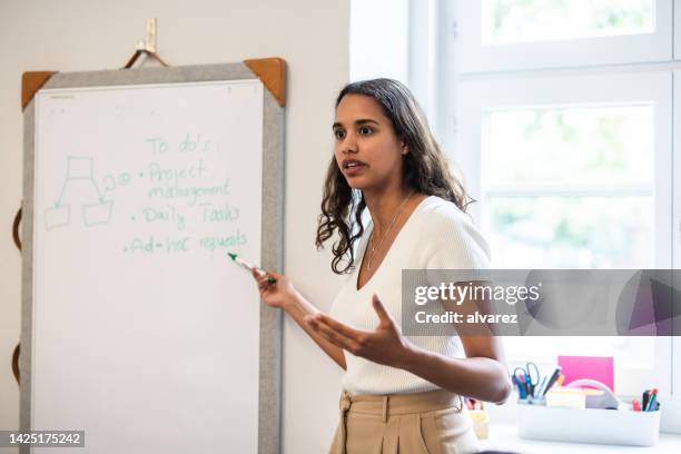 hispanic woman standing by whiteboard and giving presentation at startup office - founder stock pictures, royalty-free photos & images