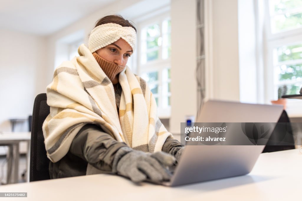 Woman feeling cold covered with a blanket using laptop in office