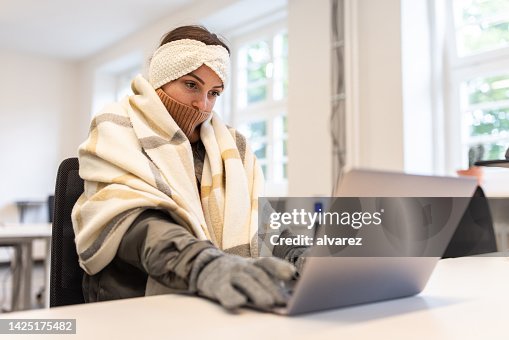 Woman feeling cold covered with a blanket using laptop in office Woman feeling cold covered with a blanket using laptop in office