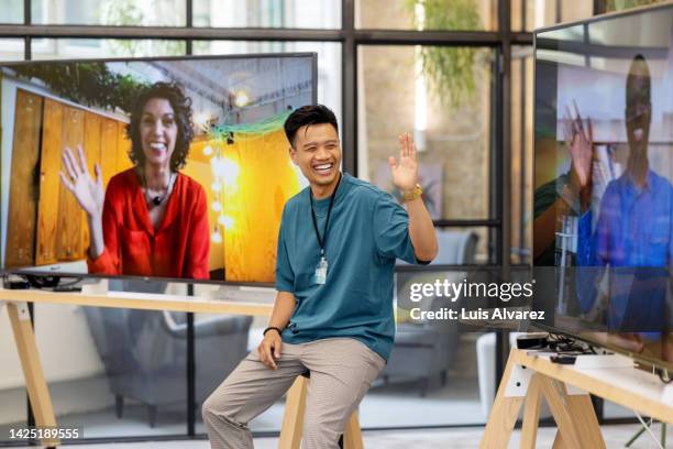 young businessman waving to colleagues on television screen during a startup conference - virtual brainstorming stock pictures, royalty-free photos & images