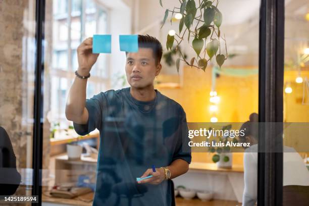 asian businessman writing on adhesive note over glass wall - pitching drawing stock-fotos und bilder