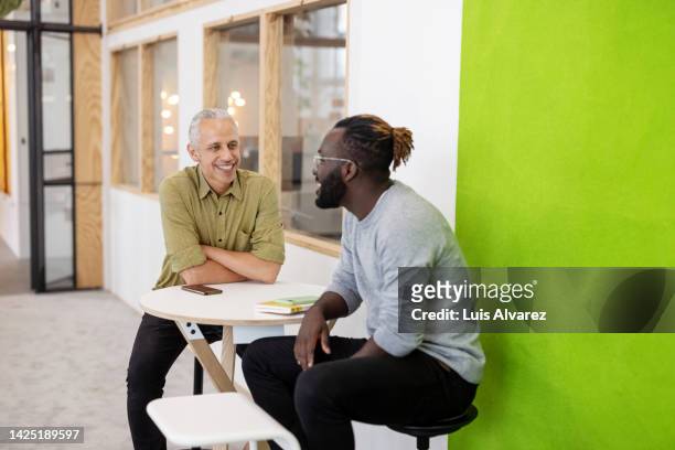 two business men sitting at table and discussing work in creative office - 2 men chatting casual office stockfoto's en -beelden