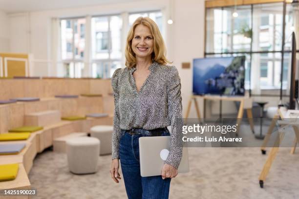 portrait of successful mature businesswoman standing in office seminar hall - grey jeans stock pictures, royalty-free photos & images
