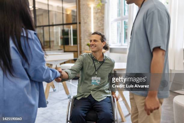 businessman in wheelchair shaking hand with female executive at a meeting - happy asian woman bright office stock-fotos und bilder