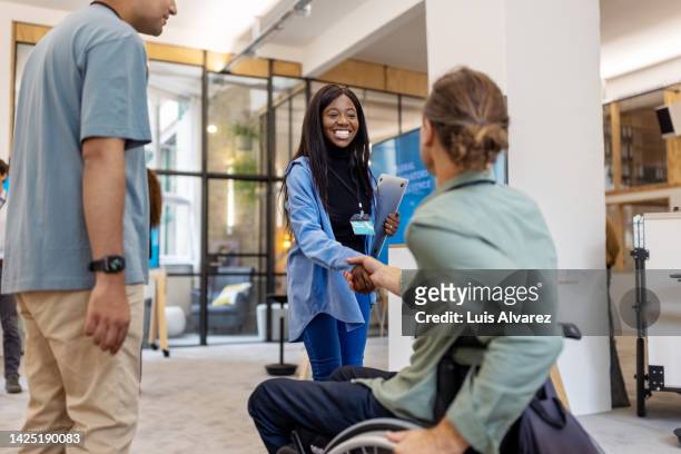 african woman shaking hands with businessman sitting on wheelchair at a conference - differing abilities female business fotografías e imágenes de stock
