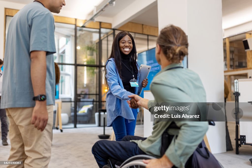 African woman shaking hands with businessman sitting on wheelchair at a conference