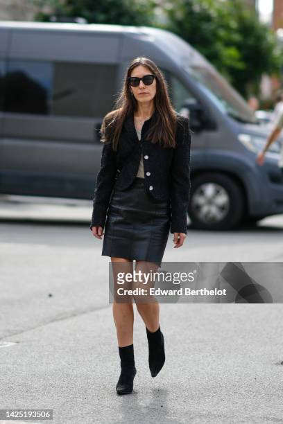 Guest wears black sunglasses, a silver long chain necklace, a black tweed buttoned / epaulet jacket, a beige tank-top, a black shiny leather short...